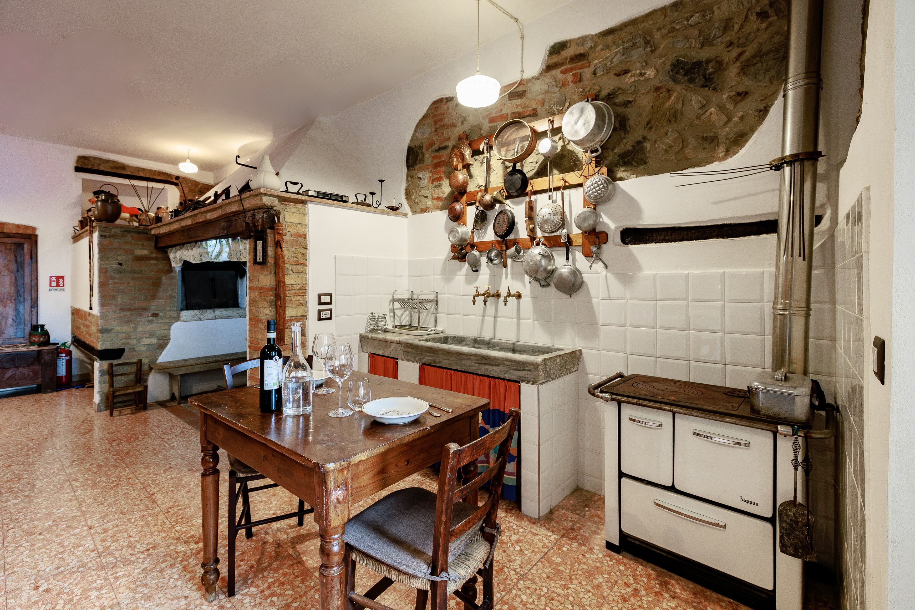 Una cucina con parete in pietra, tavolo di legno e diversi utensili da cucina appesi al muro.