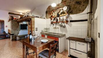 Una cucina con parete in pietra, tavolo di legno e diversi utensili da cucina appesi al muro.