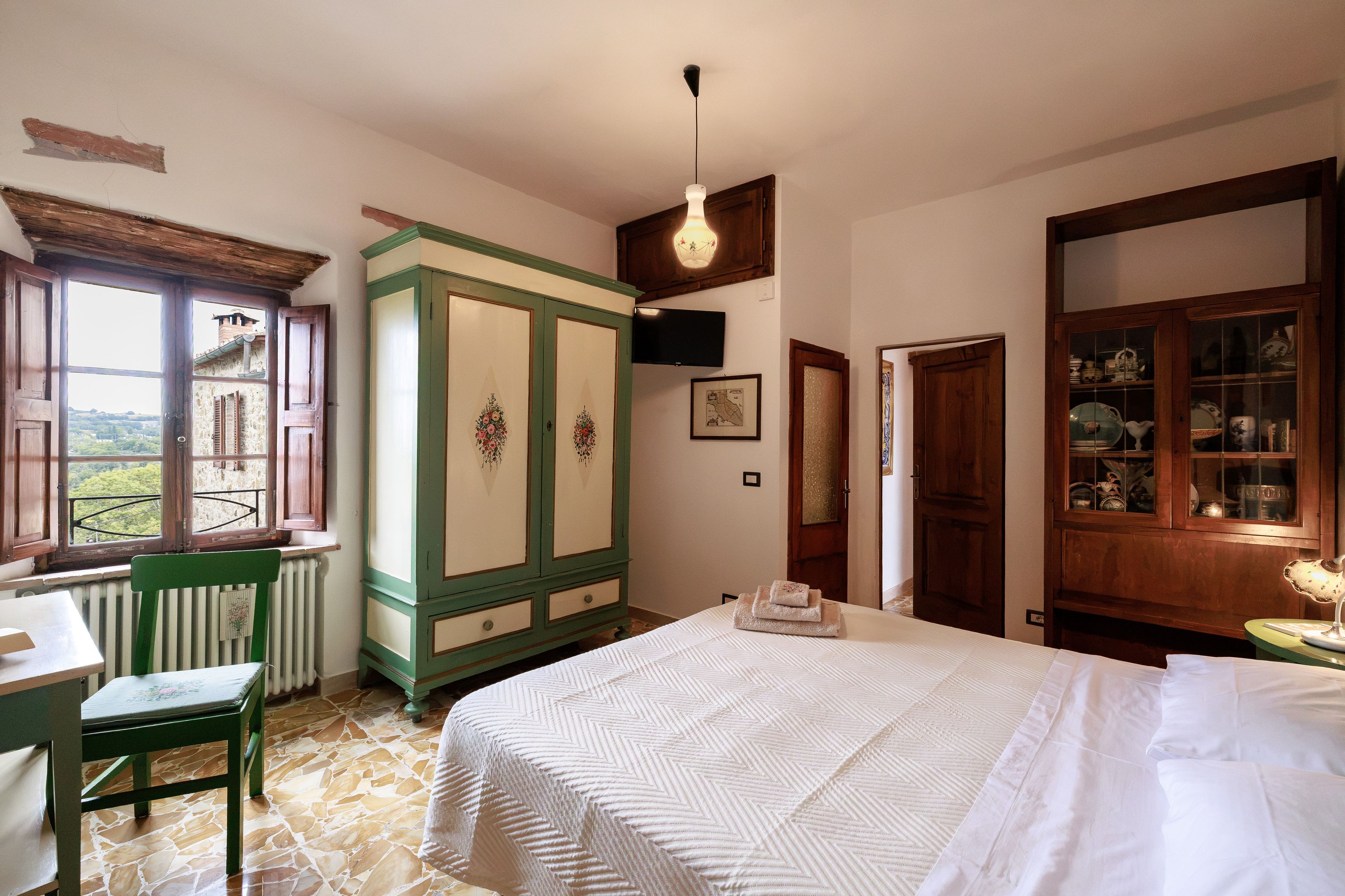 A room with a bed, a window with a view, a radiator, and a cabinet with glass doors.