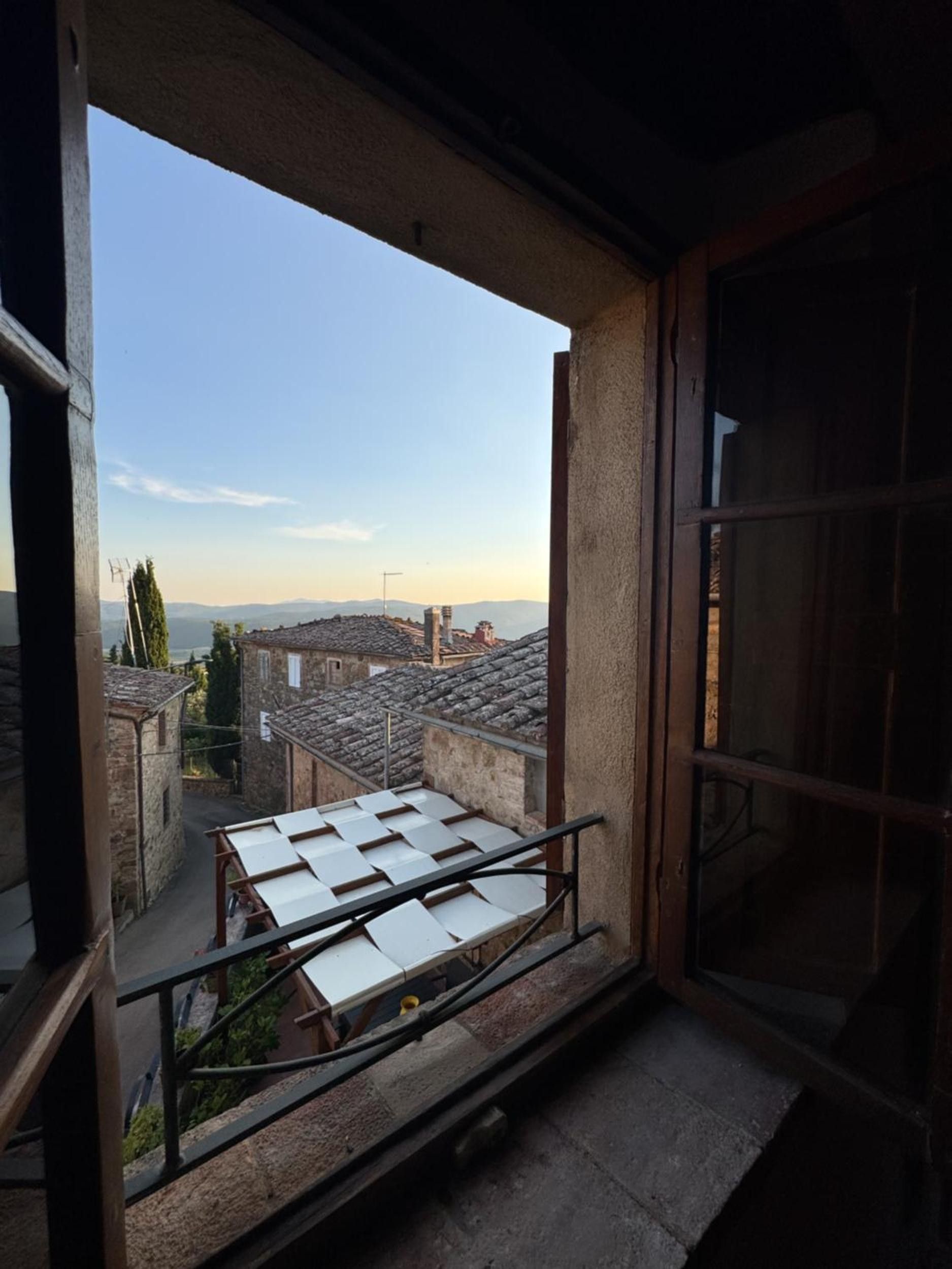 A balcony with a metal railing, a view of a town with terracotta-roofed buildings, and a clear sky.