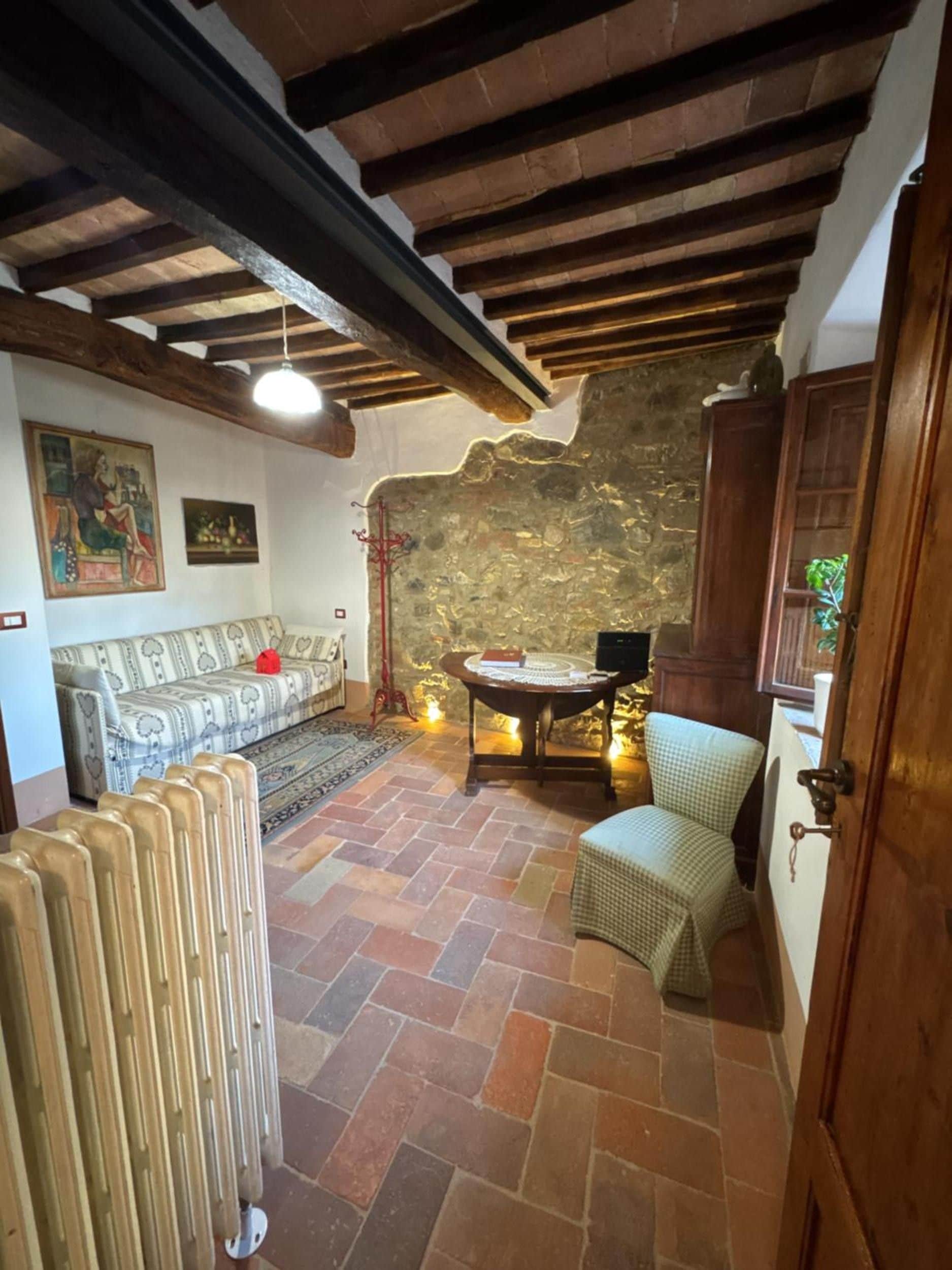 Una habitación acogedora con pared de piedra, techo de madera, un sofá, una mesa con lámpara y un radiador.