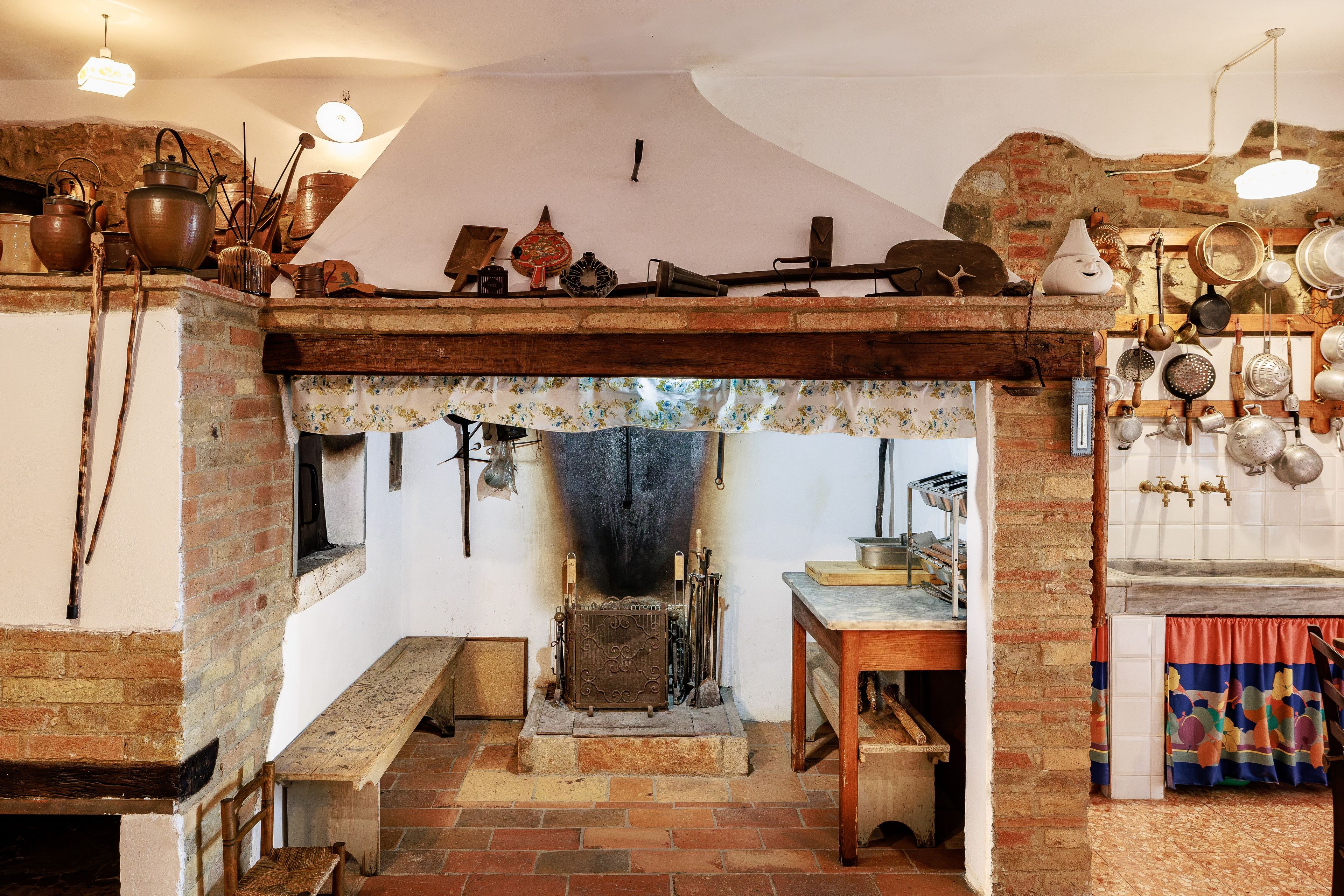 Una cucina rustica con un tradizionale stufa, pentole appese e una panca di legno.