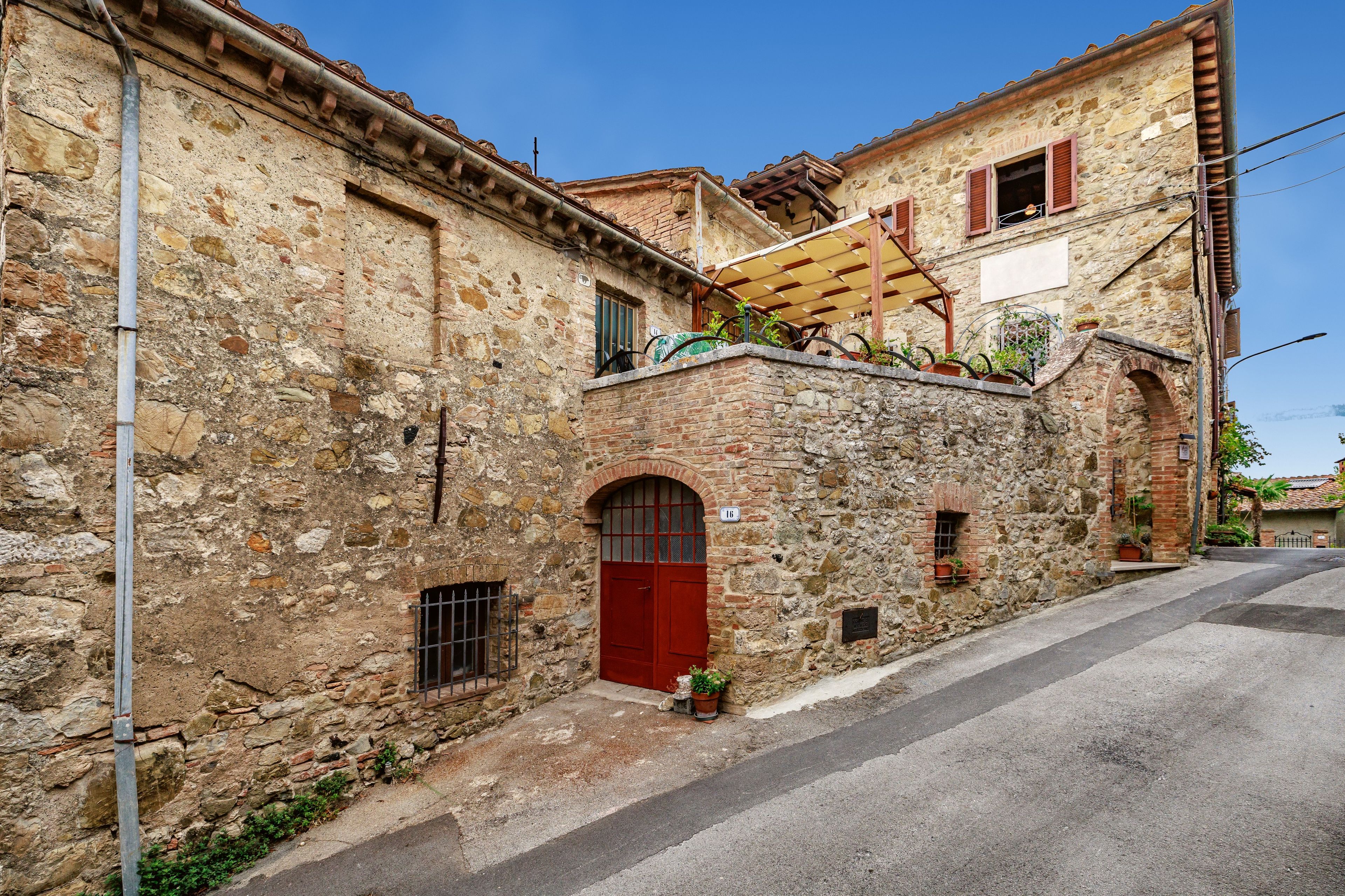 A stone building with a red door, a small window, and a balcony with plants.