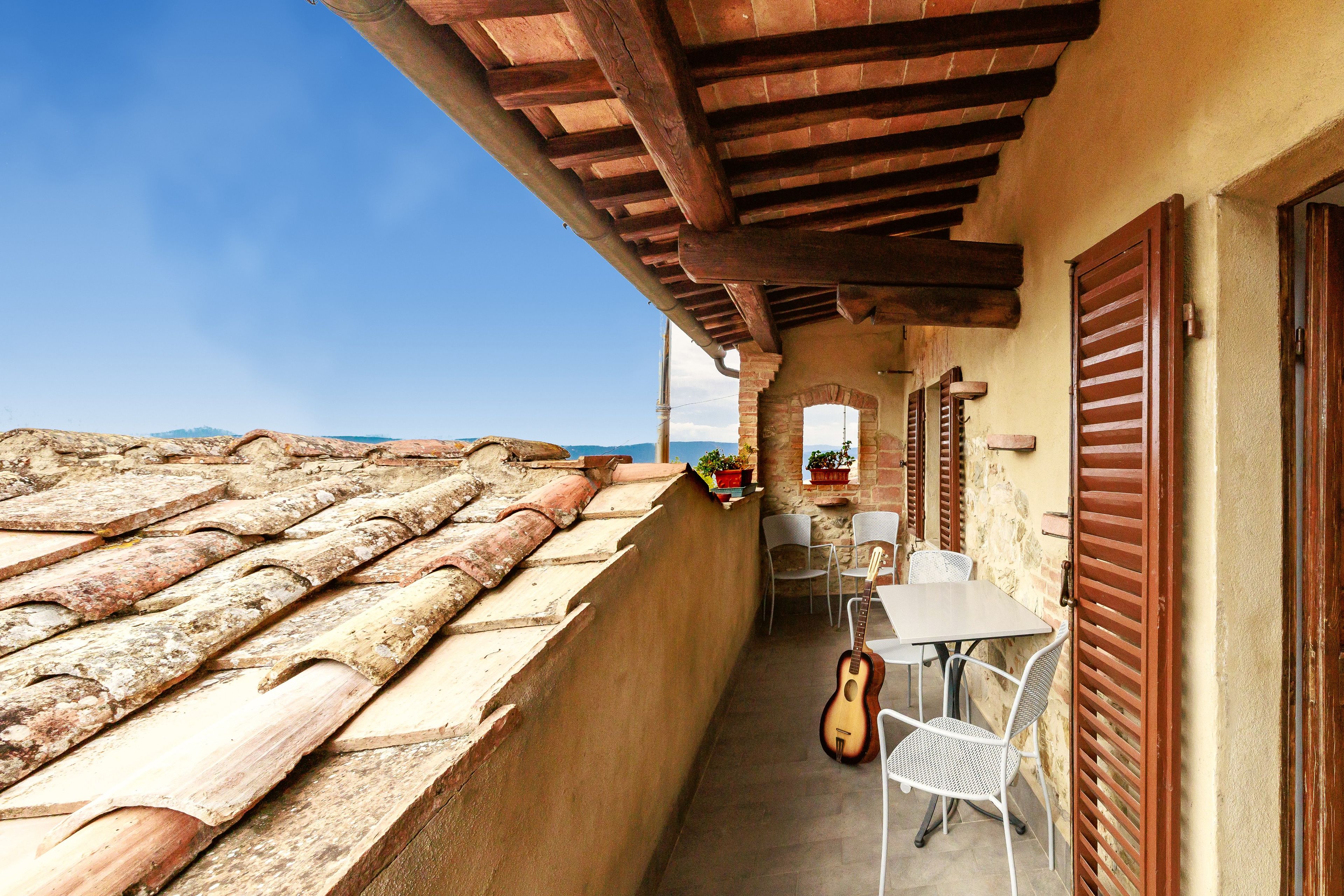 Ein Balkon mit einem Ziegeldach, einem Tisch mit Stühlen und einer an der Wand angelehnten Gitarre.