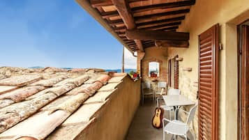 Ein Balkon mit einem Ziegeldach, einem Tisch mit Stühlen und einer an der Wand angelehnten Gitarre.