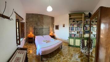 Une chambre avec un mur en pierre, un lit, une bibliothèque et un luminaire suspendu.