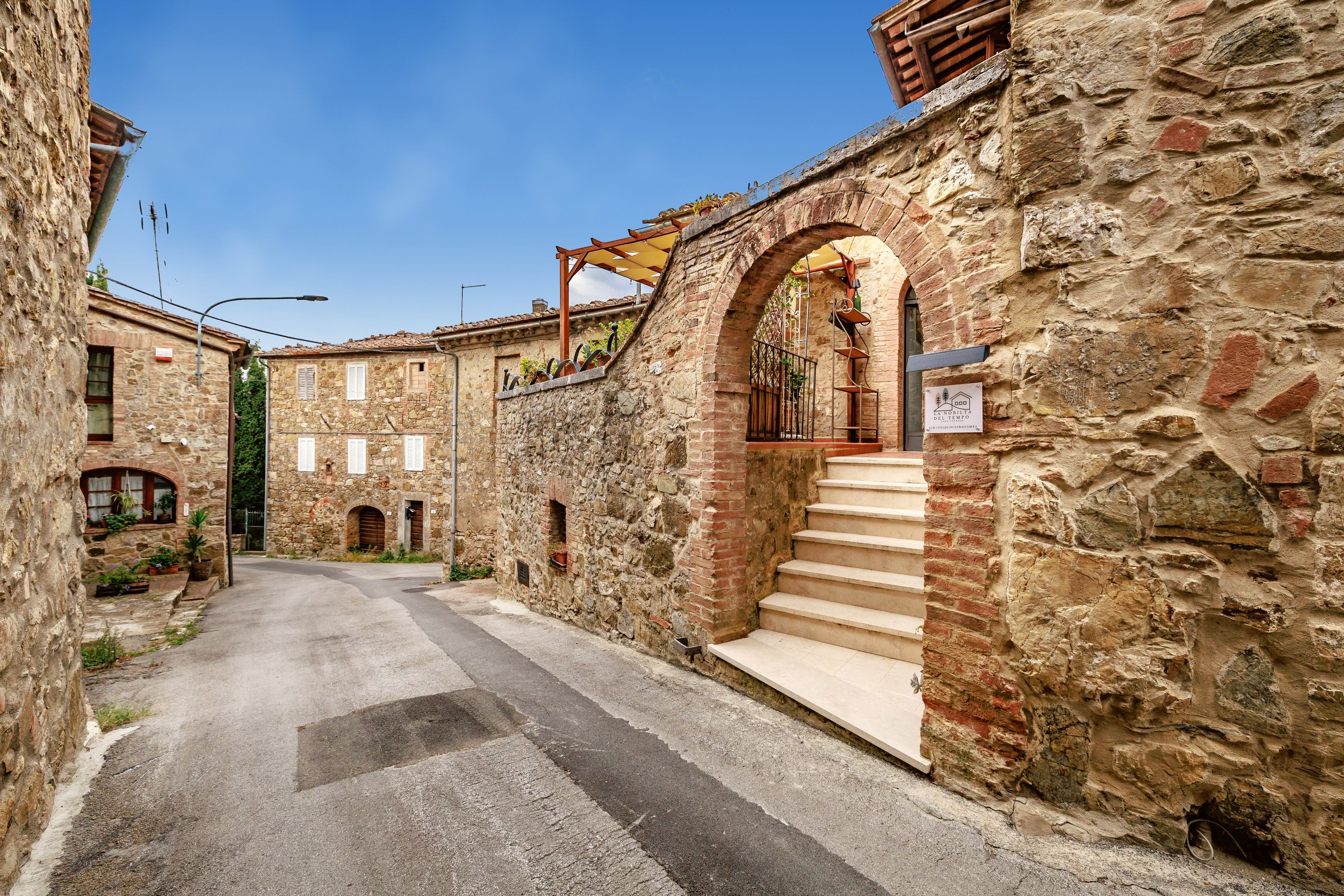 Eine enge Gasse, gesäumt von Steinhäusern mit Rundbogenöffnungen und einer Treppe, die zu einem zweiten Stock führt.