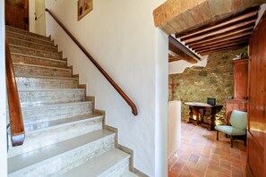 Una escala amb baranes de fusta que condueix a una habitació amb pared de pedra i una taula amb una cadira.