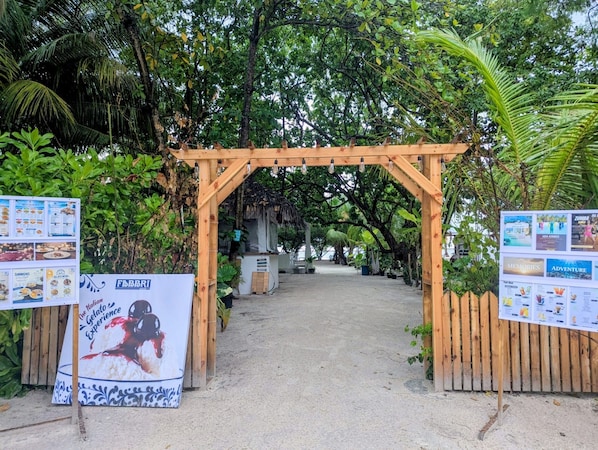 Un arco de madera que da paso a un espacio cubierto, con un tablero de menú a la izquierda y un cartel informativo a la derecha.
