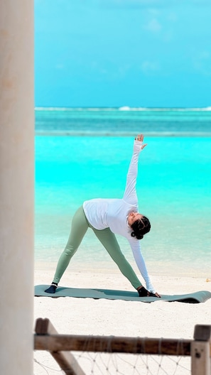 Una persona realizando una postura de yoga sobre una esterilla, con una playa y el océano al fondo.