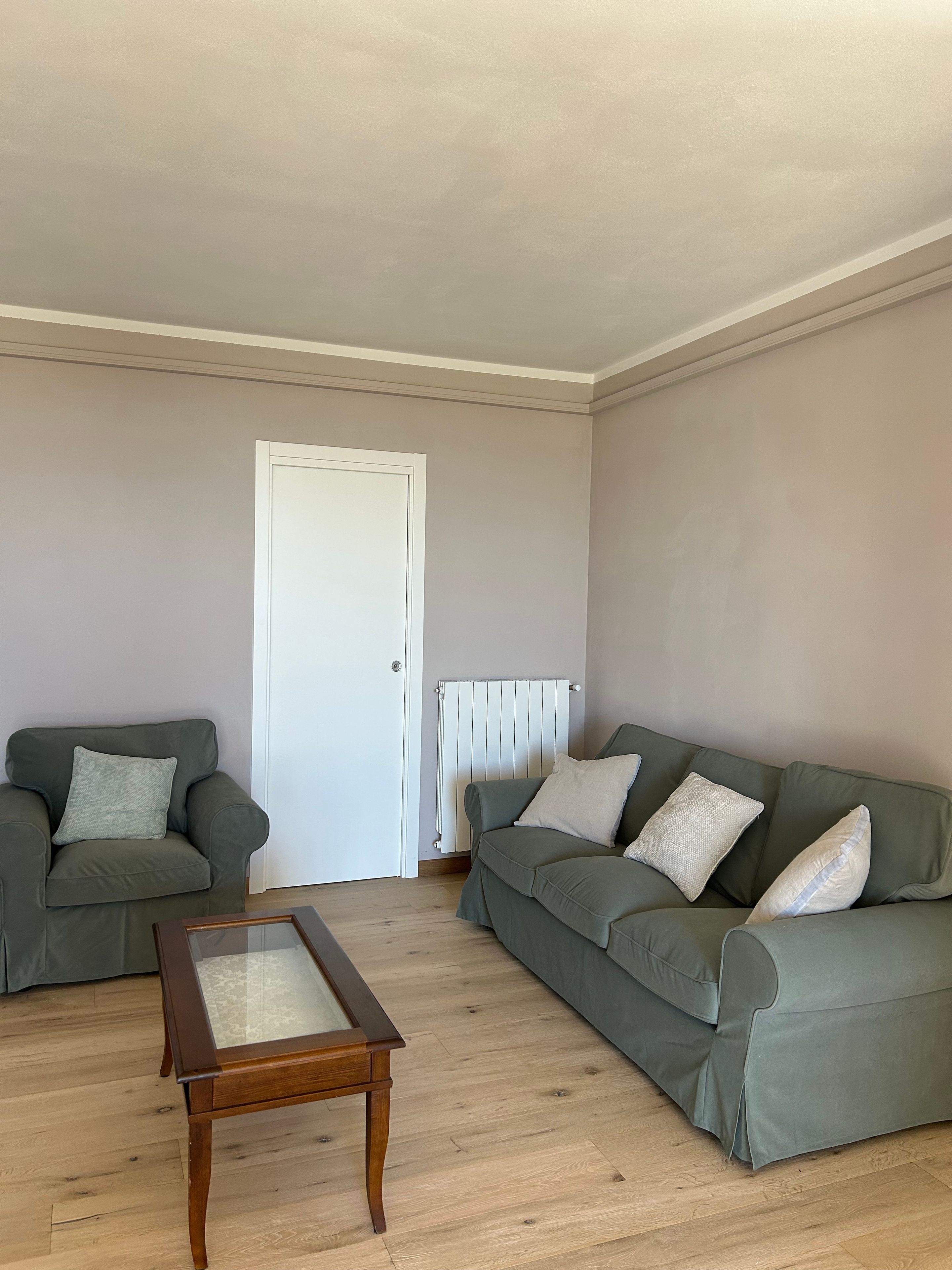 A living room with two green sofas, a wooden coffee table, and a white radiator.