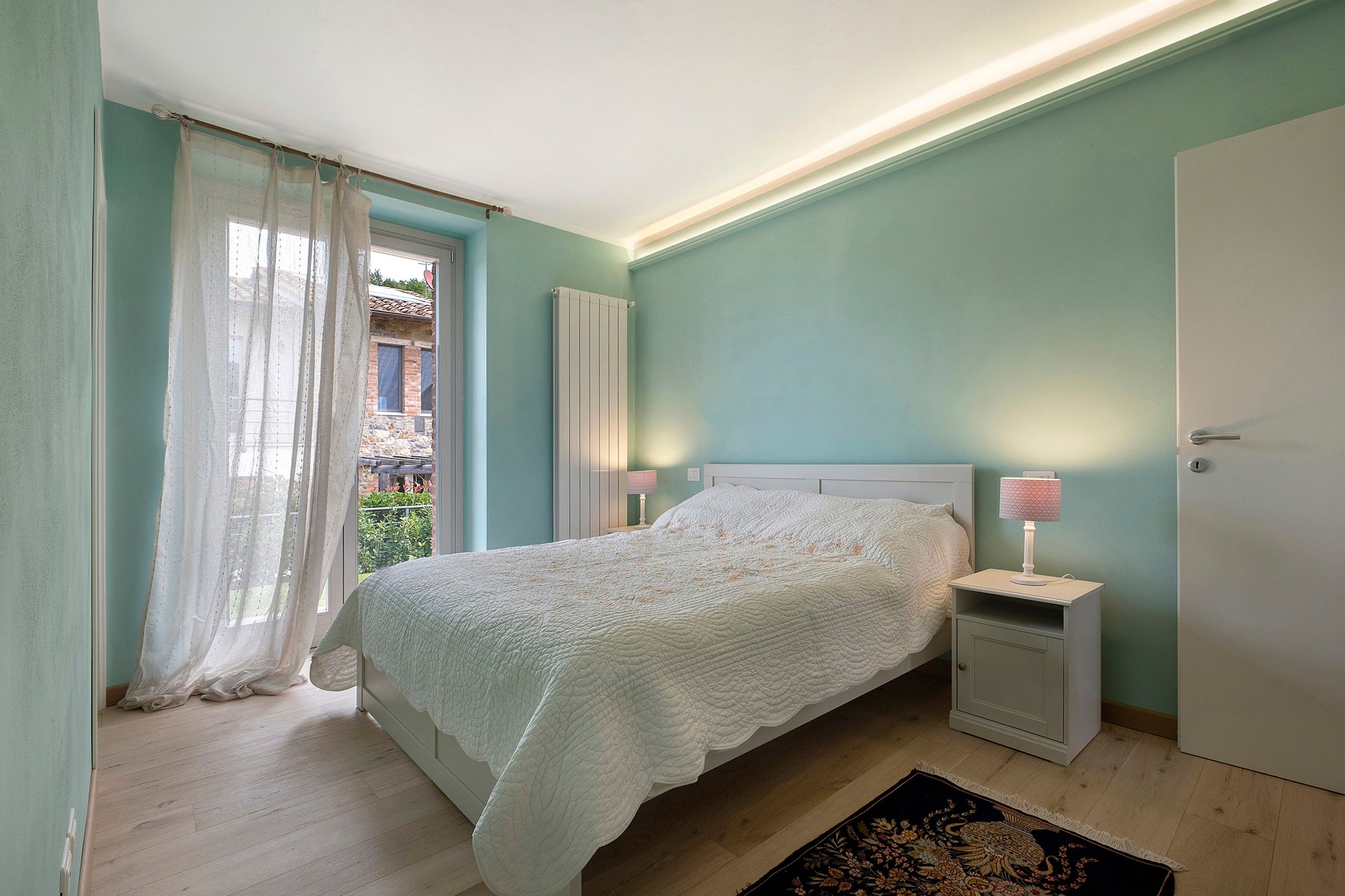 Ein Schlafzimmer mit Bett, Nachttischlampen, einer Heizung und Blick auf einen Balkon.