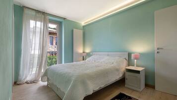 Ein Schlafzimmer mit Bett, Nachttischlampen, einer Heizung und Blick auf einen Balkon.