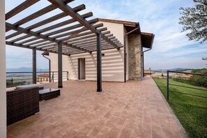 A covered patio area with a pergola, outdoor seating, and a view of the countryside.