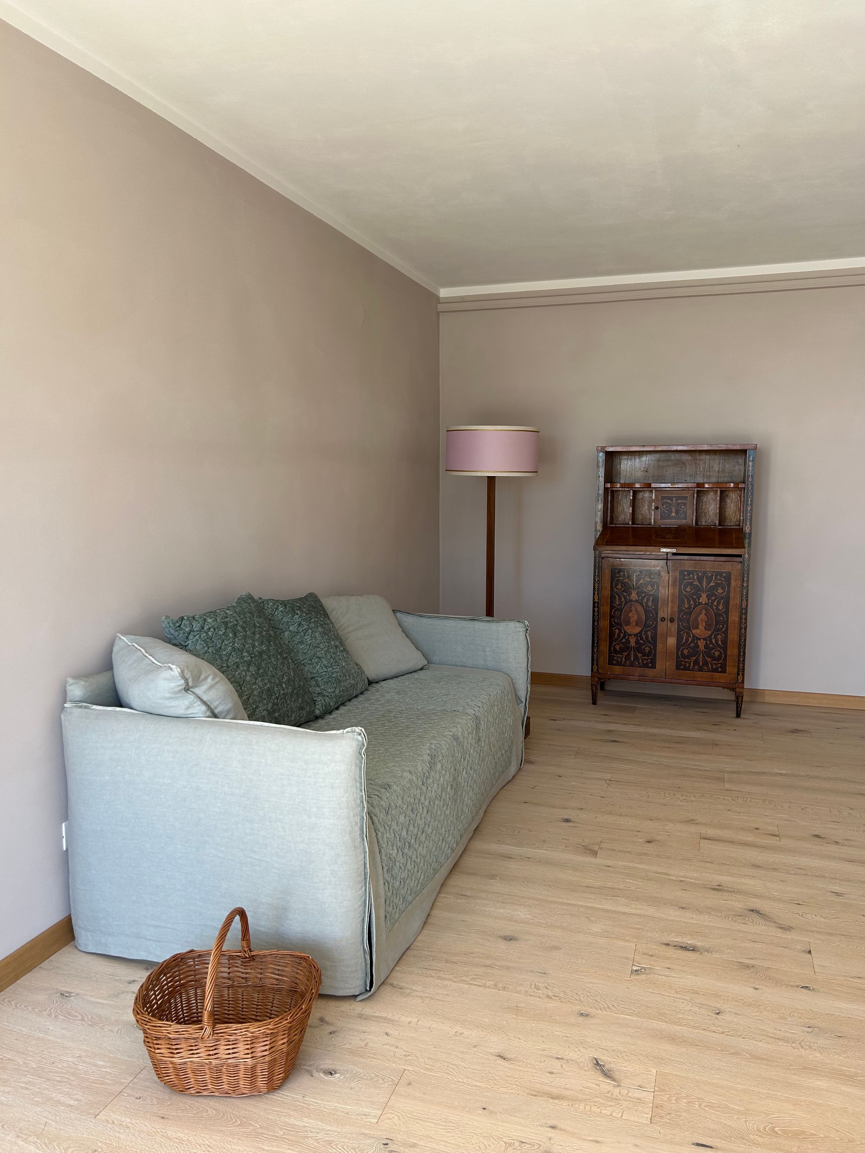 A room with a light grey sofa, a wooden cabinet, a floor lamp, and a wicker basket.