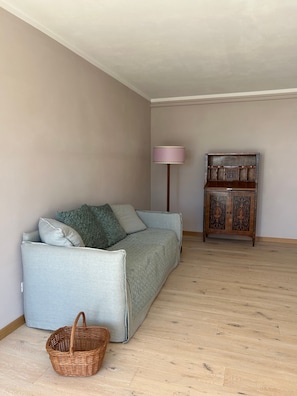A room with a light grey sofa, a wooden cabinet, a floor lamp, and a wicker basket. - Villa 'San Casciano' with Village View and Private Pool (San Casciano dei Bagni)