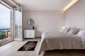 A bedroom with a bed, a nightstand, a mirror, and a view of the outdoors.