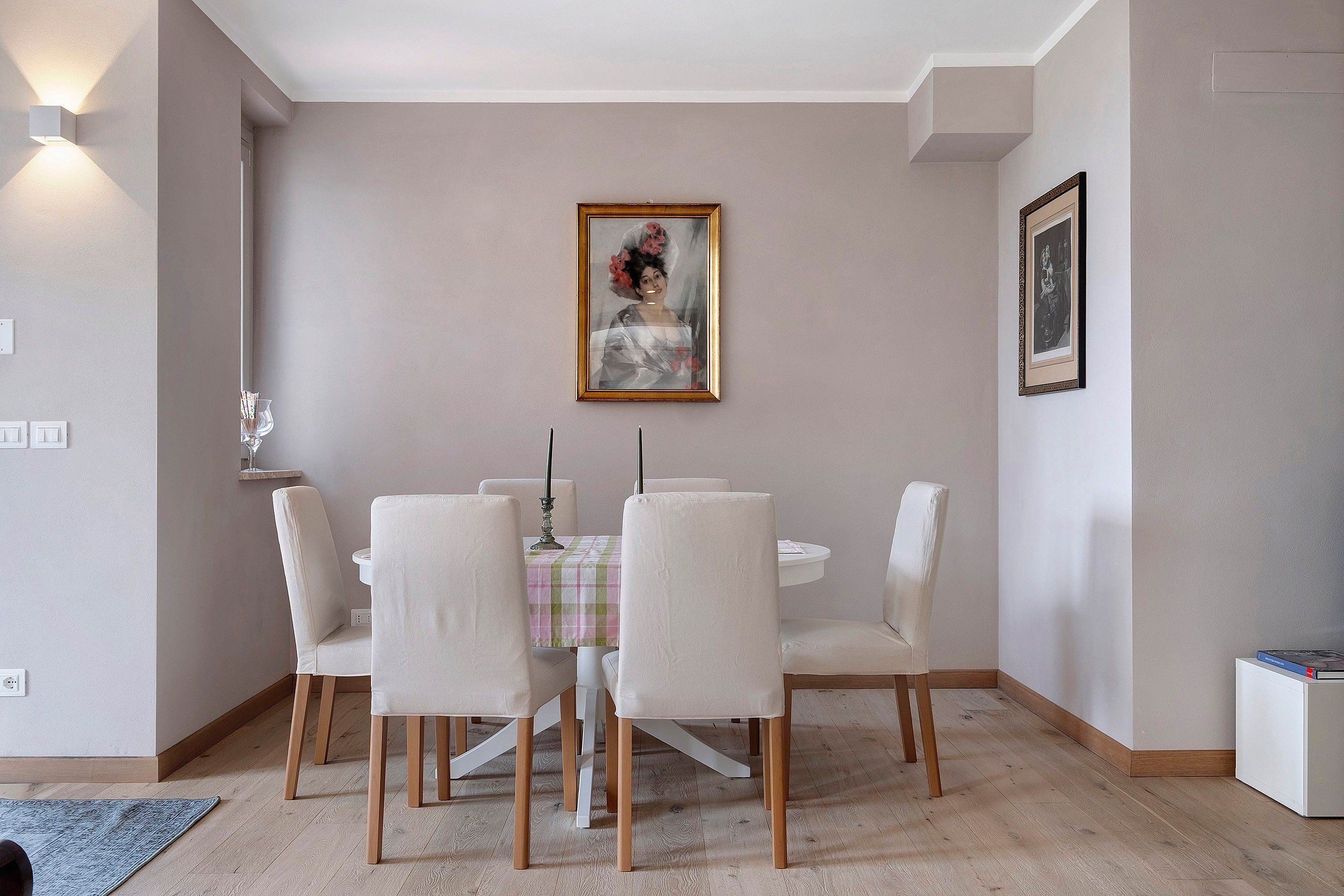 A dining area with a round table, six chairs, a painting, and a framed picture on the wall.