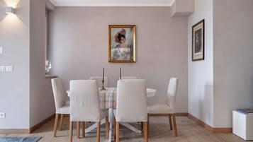 A dining area with a round table, six chairs, a painting, and a framed picture on the wall.