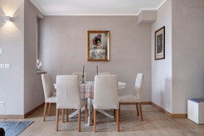 A dining area with a round table, six chairs, a painting, and a framed picture on the wall.