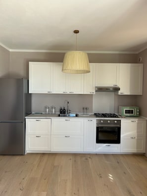 A kitchen with white cabinets, a stainless steel refrigerator, a gas stove, and a microwave. - Villa 'San Casciano' with Village View and Private Pool (San Casciano dei Bagni)