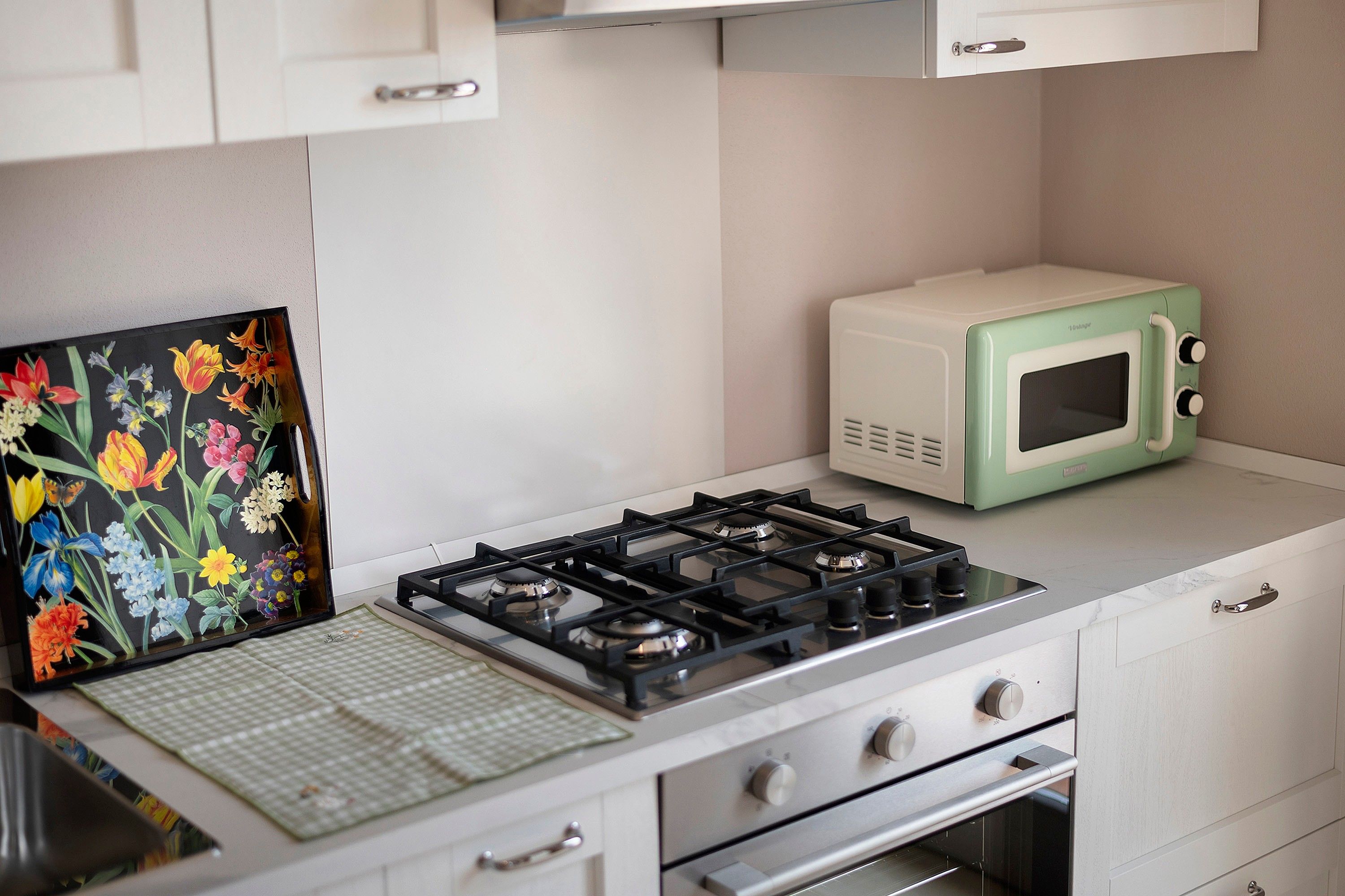 Une cuisine équipée d’une cuisinière à gaz, d’un four à micro-ondes et ornée d’un tableau représentant des fleurs au mur.