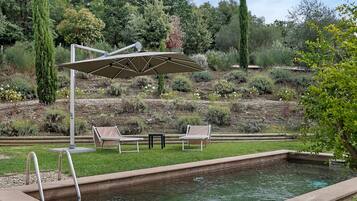 Ein Poolbereich mit einer Pergola, zwei Liegestühlen und einem kleinen Tisch.