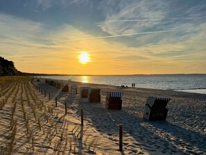 A beach with rows of beach chairs and umbrellas, a sandy path, and a sunset over the water. - Holiday Home in Glowe With Swimming Pool (Glowe)