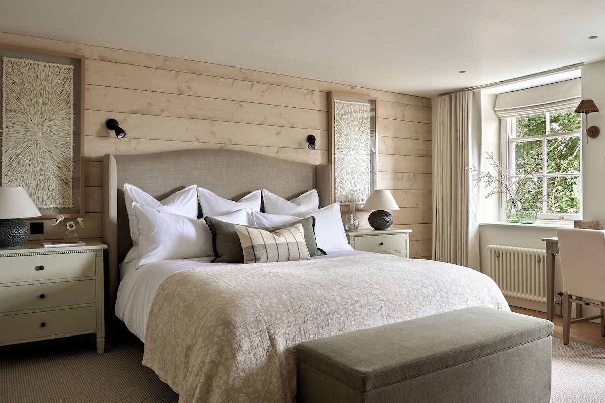 A bedroom with a large bed, two bedside tables, a chair, a window with curtains, and a radiator.