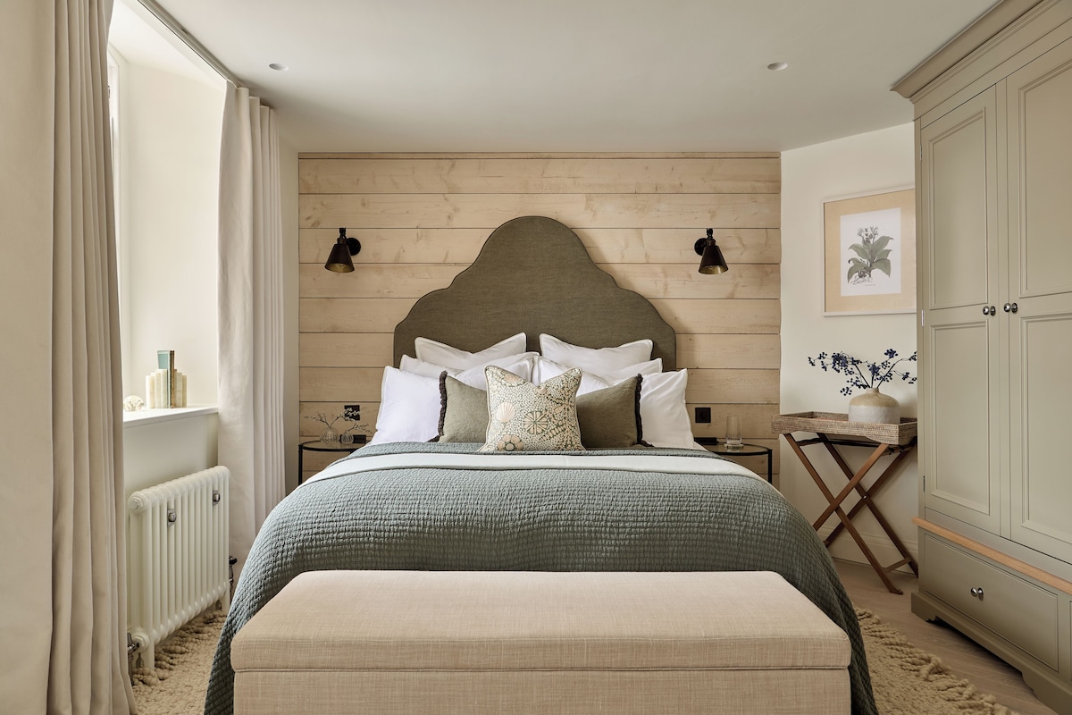 A bedroom with a wooden headboard, a bed with multiple pillows, a bedside table with a lamp, and a radiator.