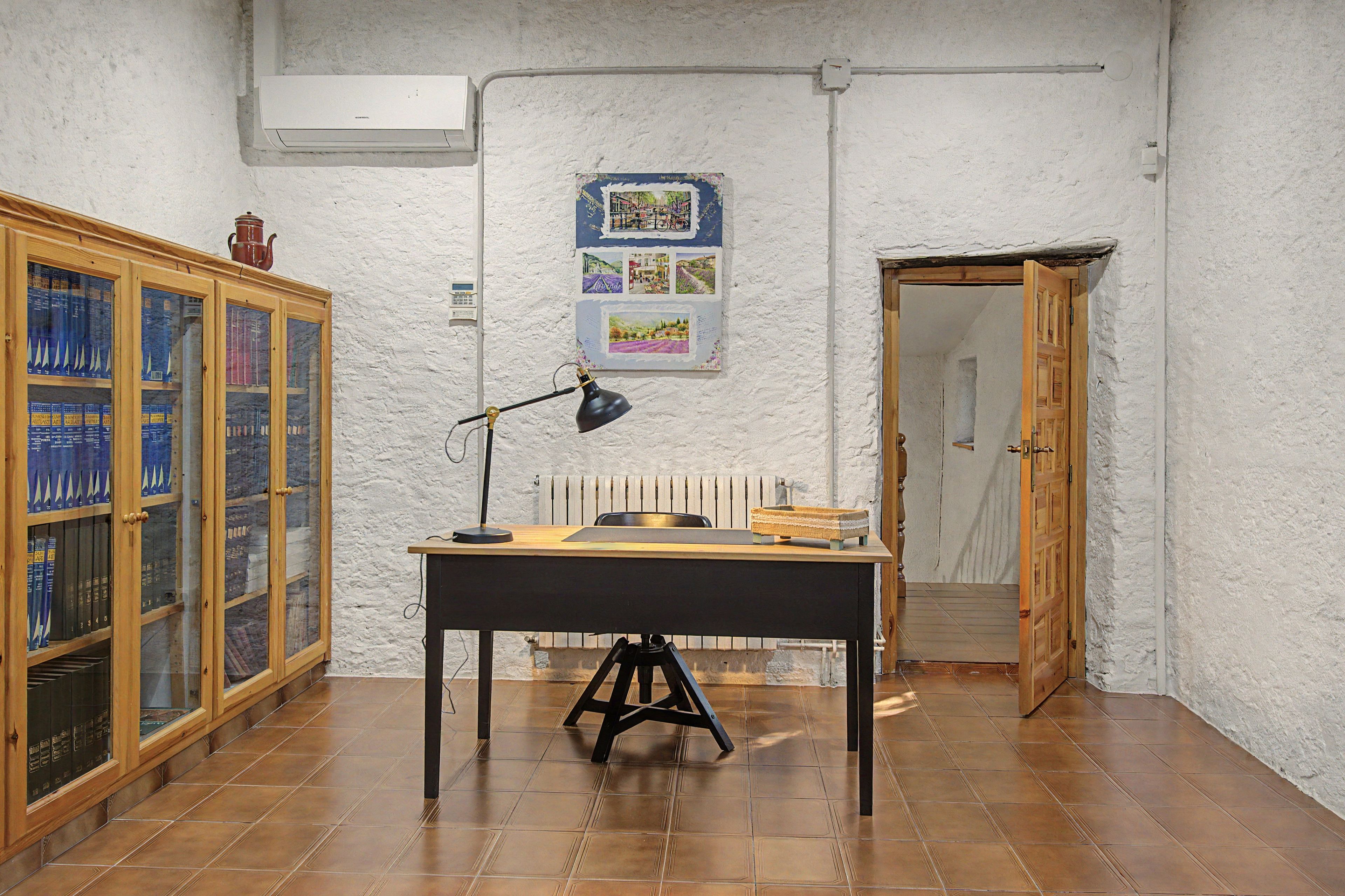 Una sala de estudio con escritorio, lámpara, radiador y un mueble de madera lleno de libros.