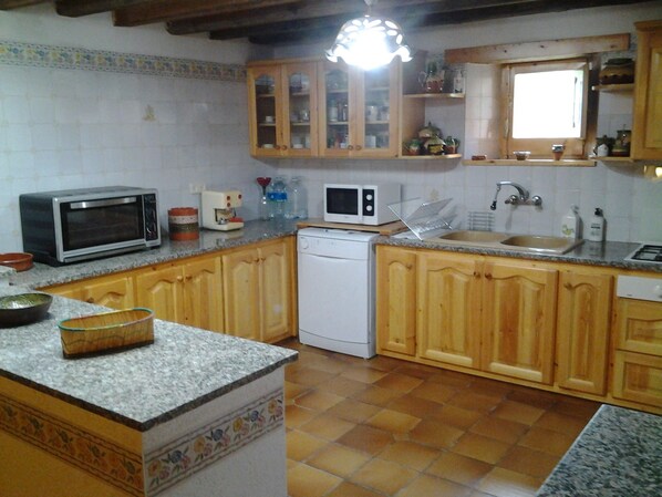 A kitchen with wooden cabinets, a microwave, a dishwasher, and a sink. - Holiday Home 'Masia De Can Creus 1890' (Girona)
