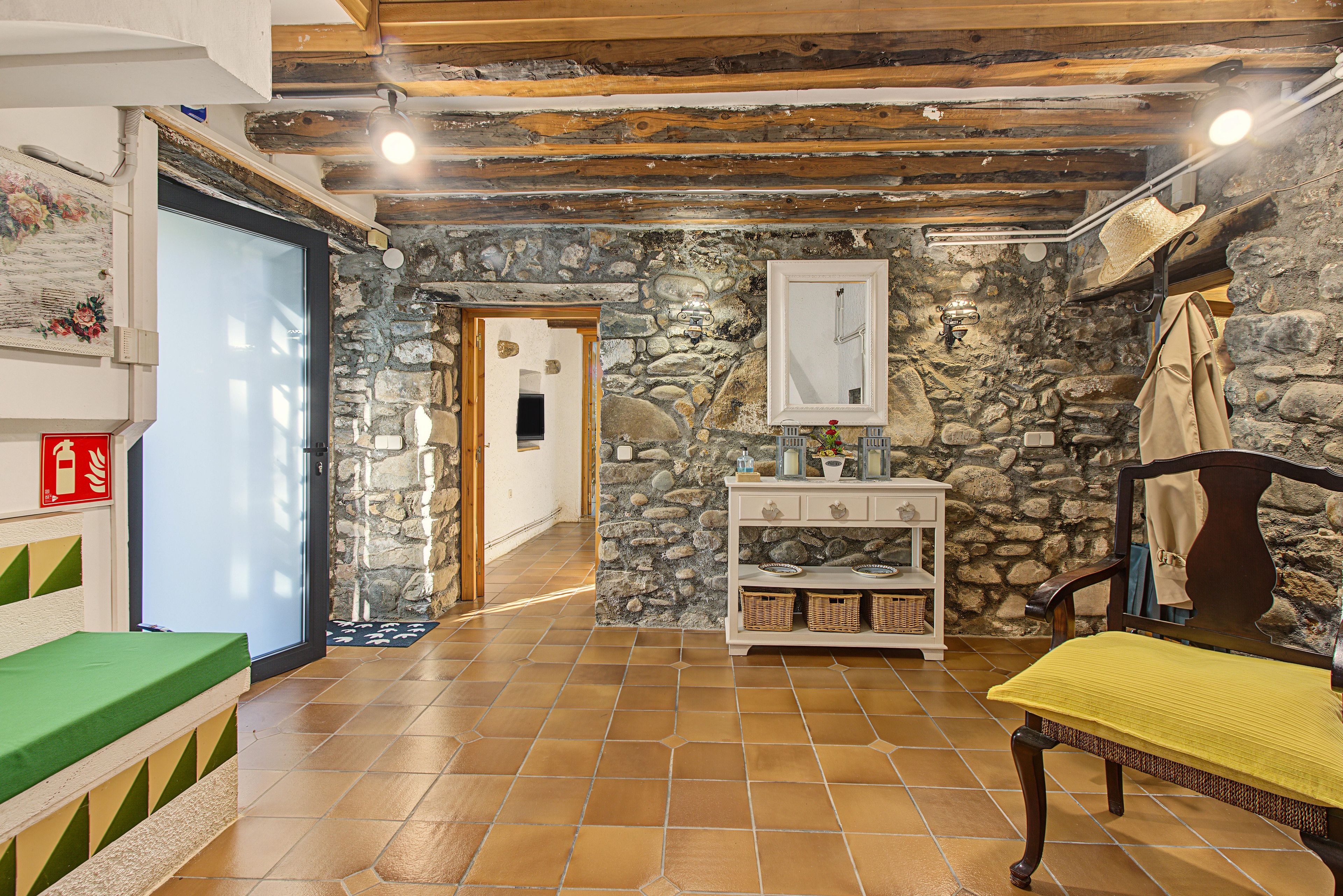A room with a stone wall, a wooden bench, a table with a yellow tablecloth, and a door leading to another room.