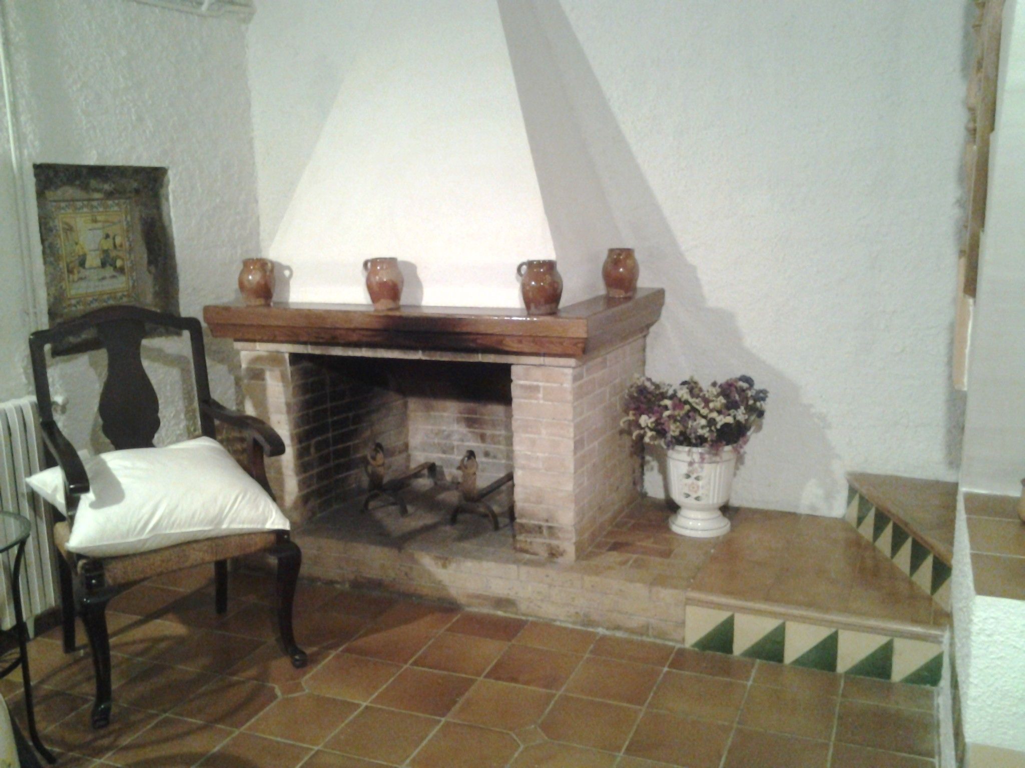 Ein Zimmer mit Kamin, einem Sessel und einem kleinen Tisch mit einer Vase.