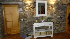 A stone wall with a wooden door and a white console table with baskets and a mirror. - Holiday Home 'Masia De Can Creus 1890' (Girona)