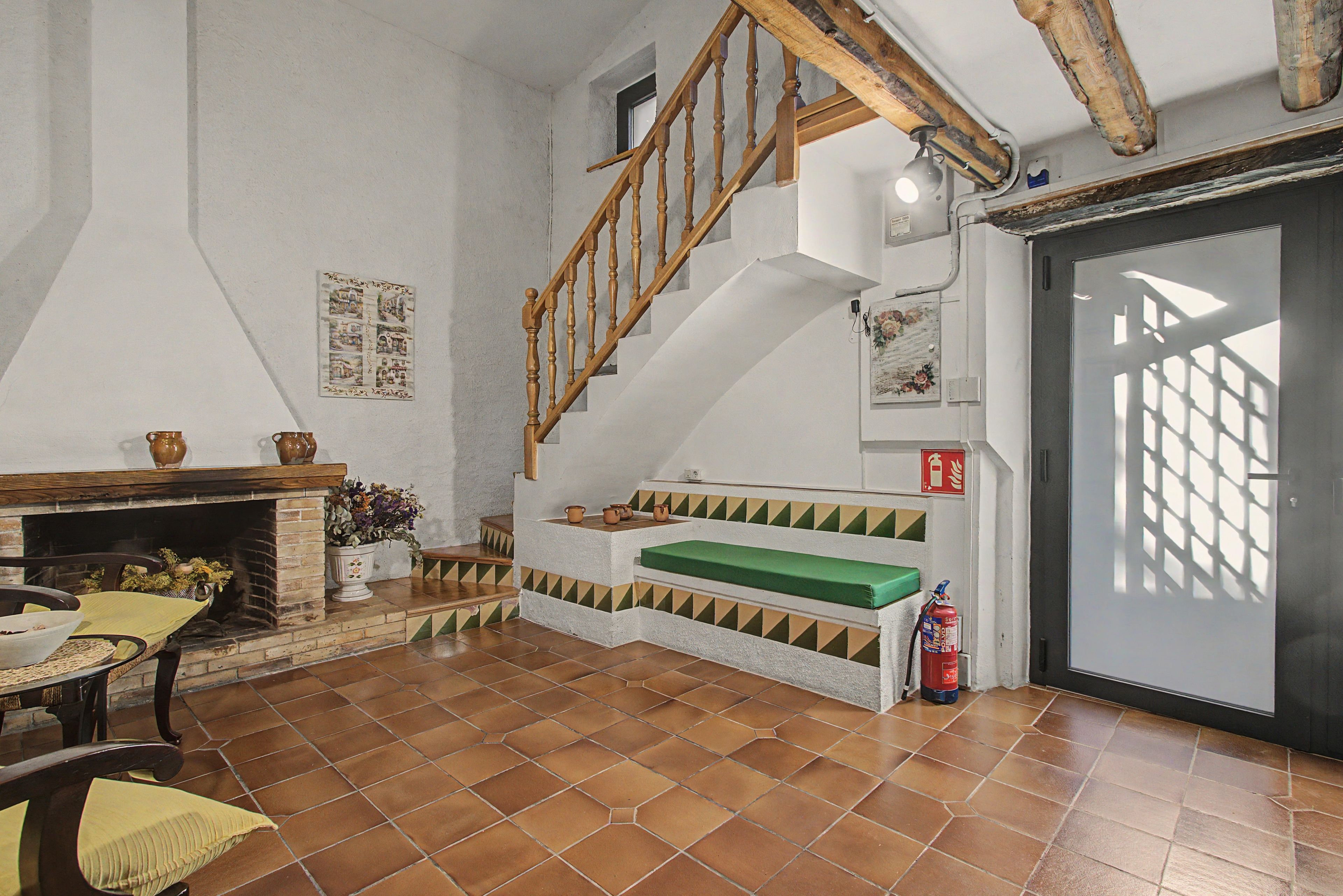 Un intérieur rustique avec un escalier en bois, une cheminée et un banc vert.