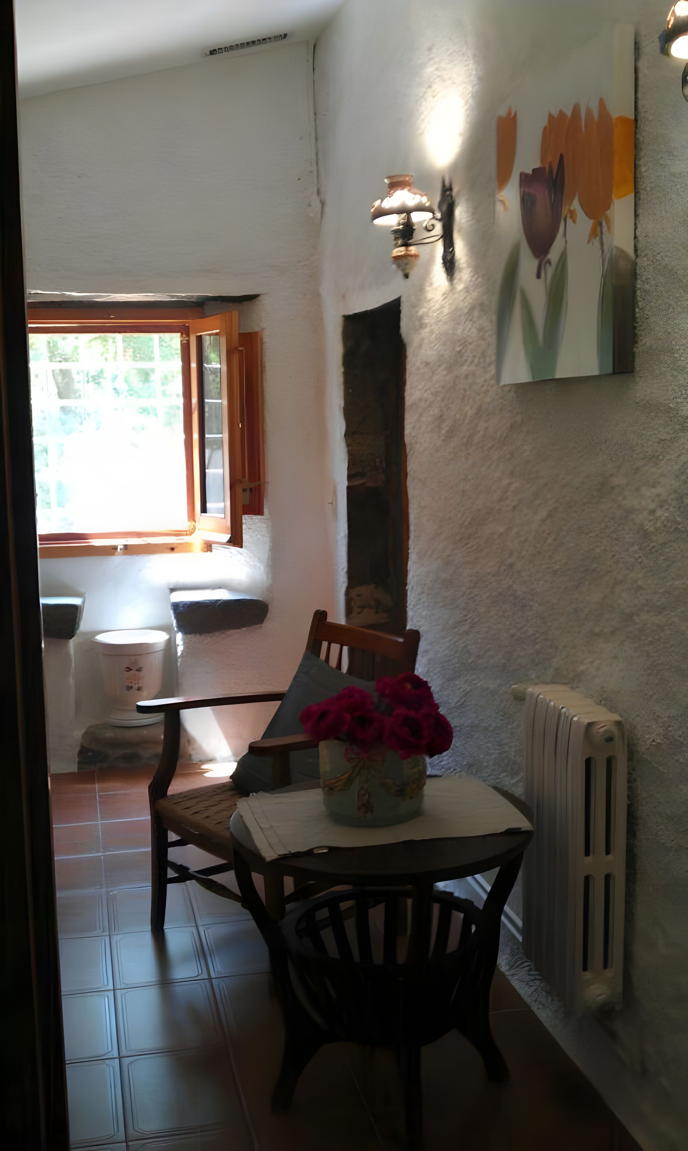 Uma sala de jantar com mesa, cadeiras, um vaso com flores, um radiador e um quadro na parede.