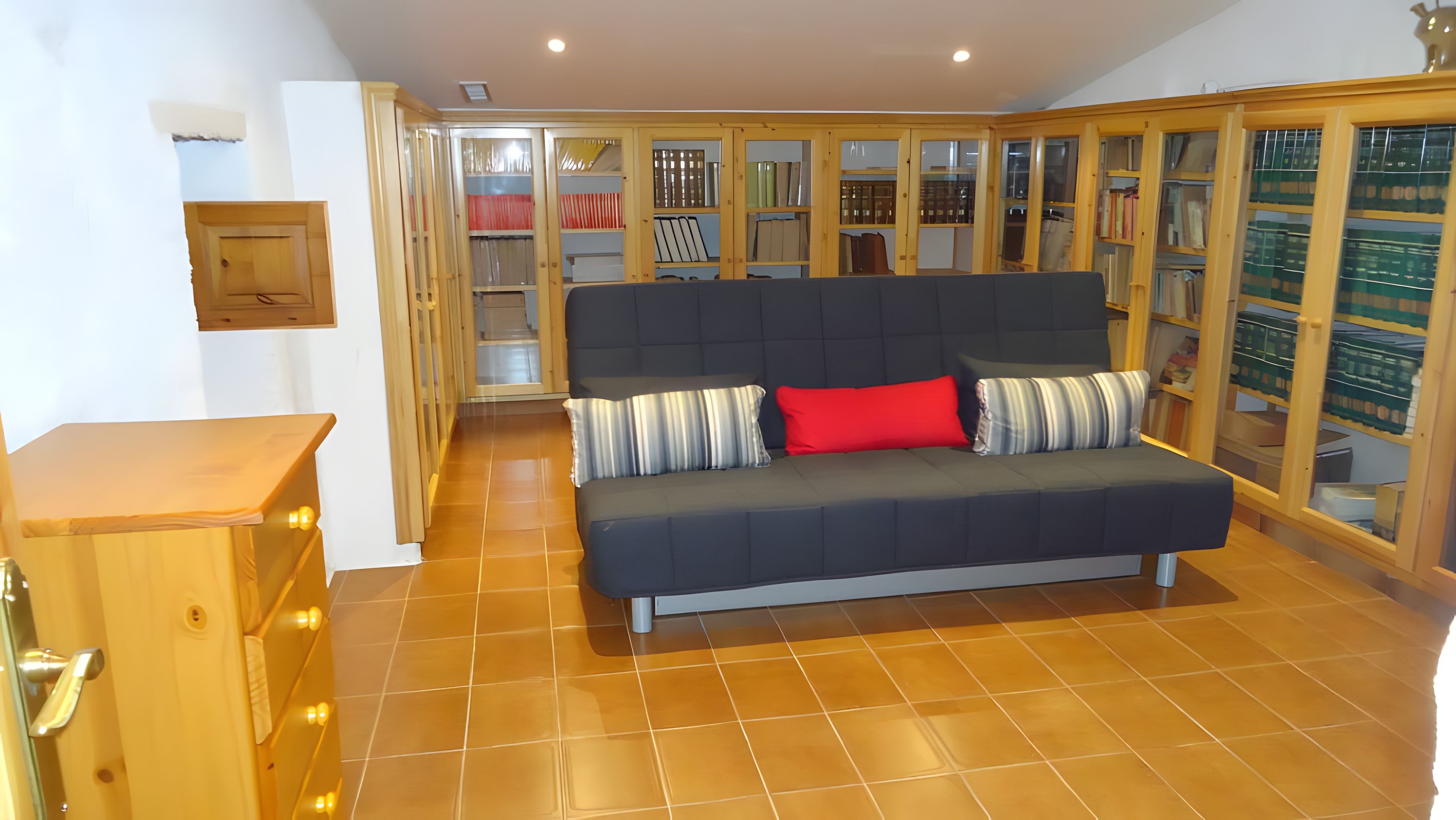 Ein Zimmer mit einer Couch, einem Holzschrank und einem Fliesenboden.