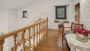 A staircase with wooden balusters leading to a landing with a table and chair, a window with a view, and a small shelf with decorative items.