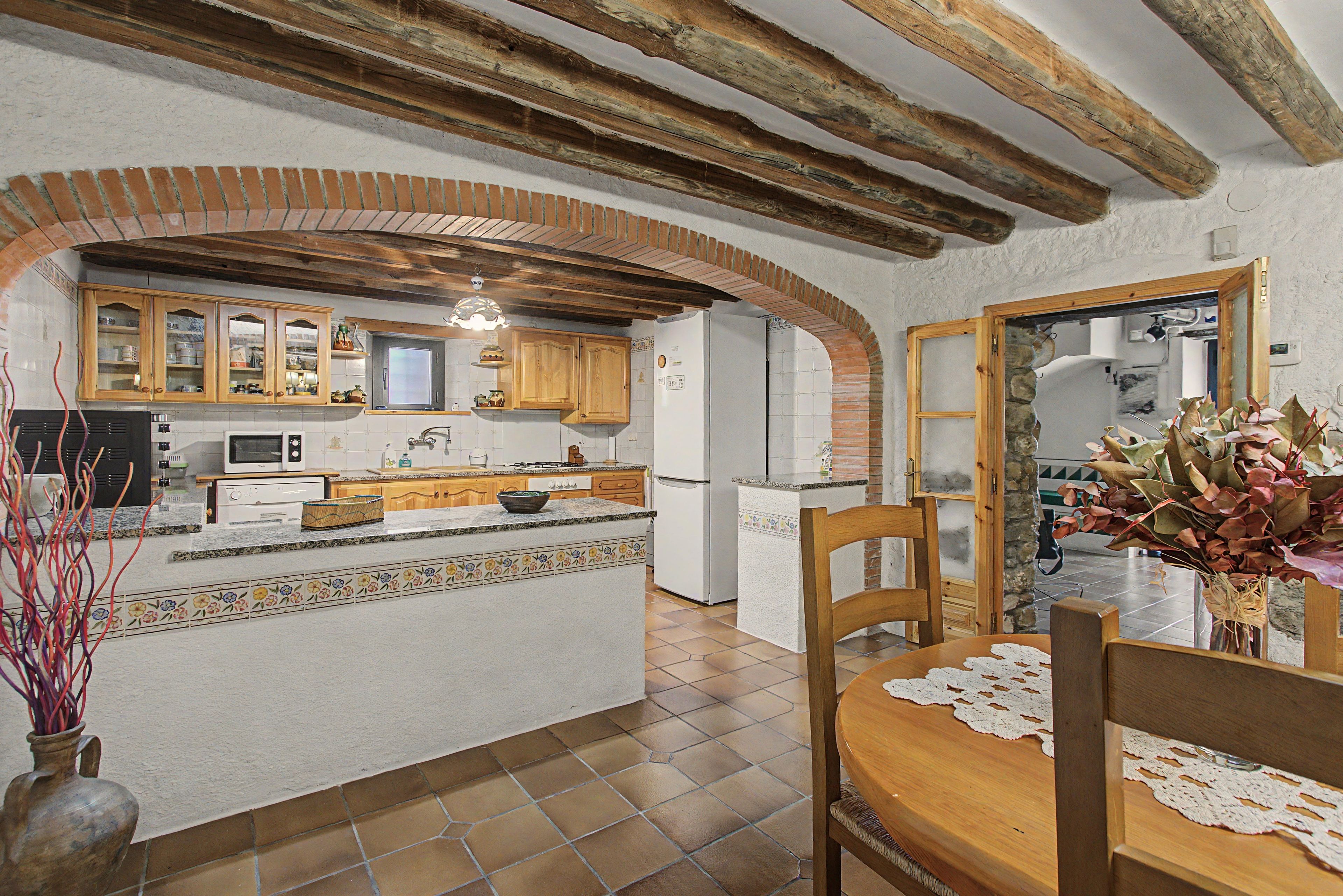 Une cuisine dotée d’un îlot central, de meubles en bois et d’une arche en pierre.