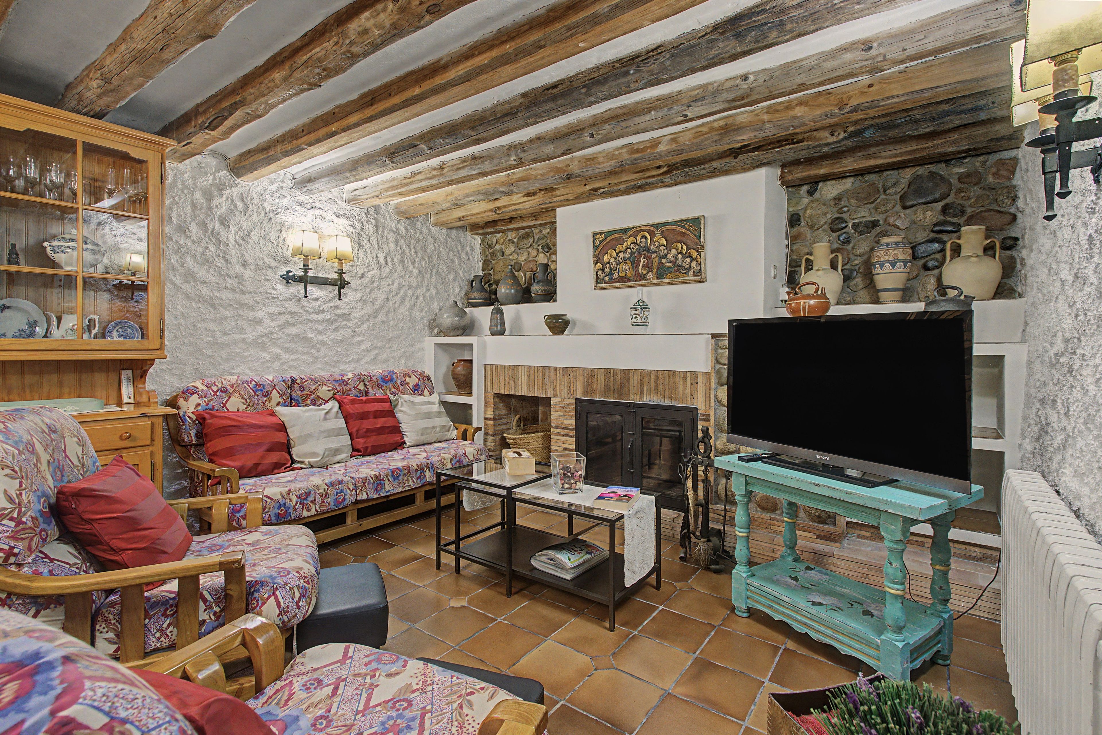 Una sala de estar rústica con vigas de madera a la vista, un conjunto de sofás, un televisor y una pared de piedra.