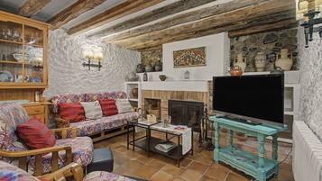 A rustic living room with exposed wooden beams, a sofa set, a television, and a stone wall.