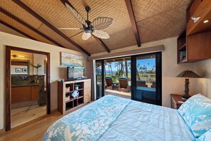 A bedroom with a large bed, a ceiling fan, a TV, and a view of palm trees and a beach. - Expansive Ocean Views in Puamana 48-3 (Lahaina)