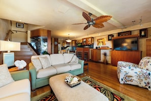 A spacious living room with a sofa, a patterned armchair, a television, and a ceiling fan. - Expansive Ocean Views in Puamana 48-3 (Lahaina)