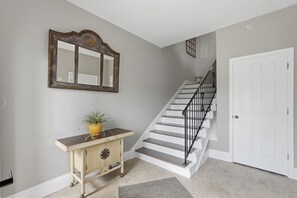 Una escalera con una puerta blanca al final, una consola de madera con una planta en maceta y un espejo grande en la pared.