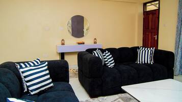 A living room with two black sofas, one with striped pillows, a round mirror, a small table, and a door with a window.