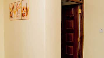 A hallway with a door leading to a room, a tiled floor, and a rug with slippers.