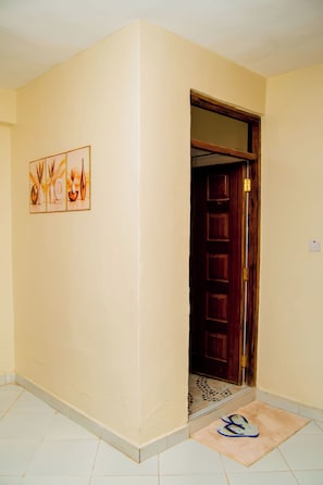 Un pasillo con una puerta que da a una habitación, piso de baldosas y una alfombra con pantuflas.