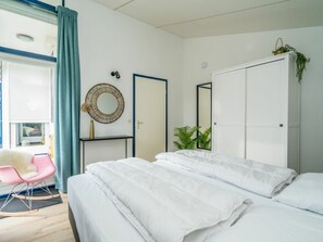 A bedroom with a bed, a wardrobe, a mirror, a chair, and a window with curtains. - Holiday Home in Renesse With Swimming Pool (Renesse)