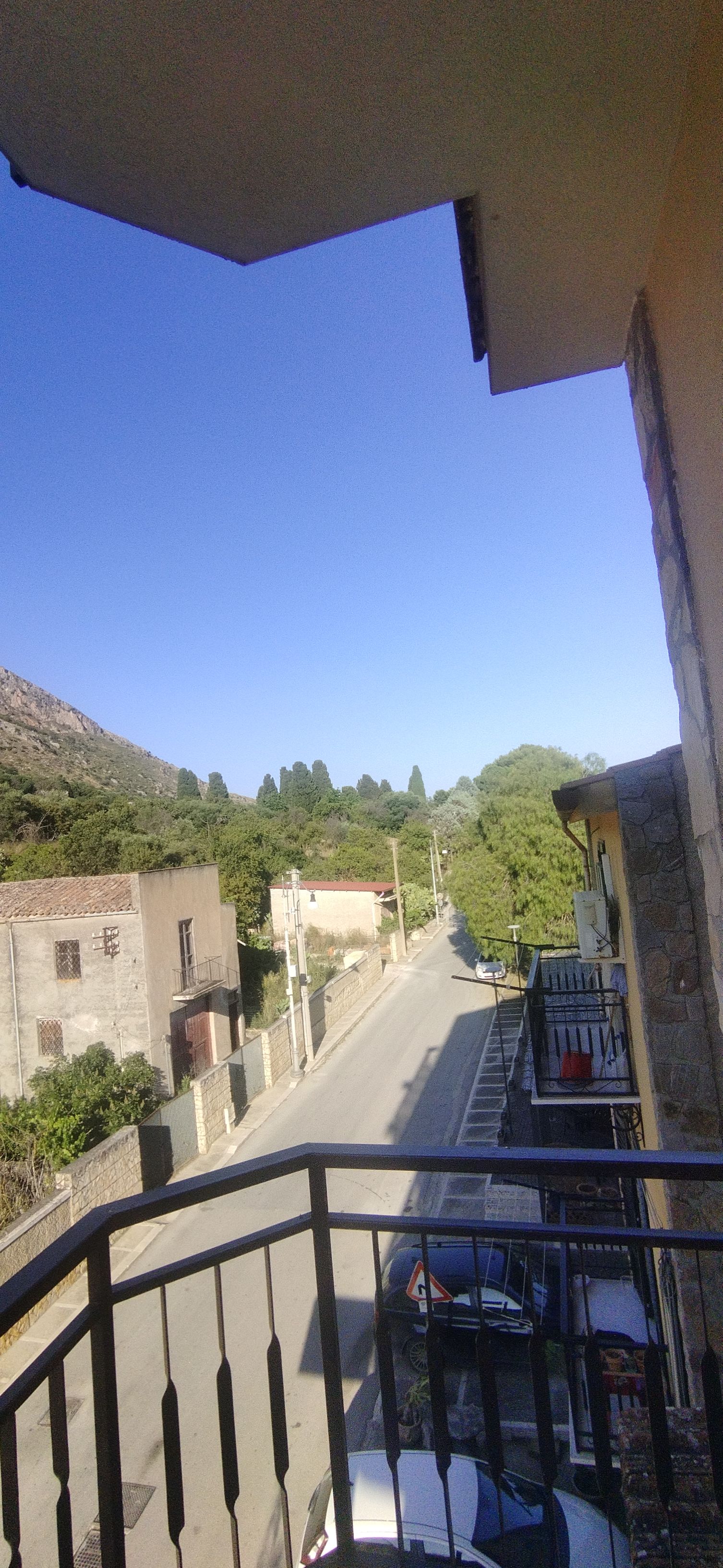 Un balcón con vista a una calle y edificios, un coche estacionado en la calle y un cielo azul despejado.